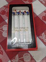 Full view of unopened original box containing four Georges Briard glass swizzle sticks with clown tops.