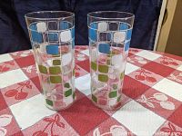 Two identical tall iced tea tumblers with softly rounded square patterns in blue, green, and white on a clear glass body, shown side by side.