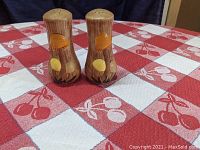 Front view of both mushroom-themed salt and pepper shakers on red and white tablecloth, showing hourglass shape and colorful mushroom mold.