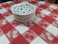 Stack of eight white ceramic cereal bowls with blue floral design from Myott Finlandia on a red and white checkered tablecloth.