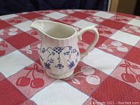 Side view of Myott Finlandia cream colored porcelain creamer with blue floral decoration, showing handle and spout