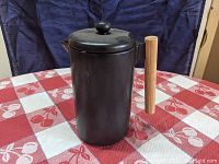 Black porcelain French press with wooden handle and lid knob, shown from a side angle on a red and white checkered tablecloth.