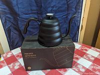 Front side view of black Soulhand pour over coffee kettle on original box, showing ribbed design and built-in thermometer on lid.