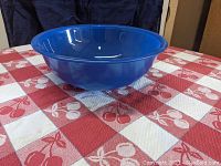 Side angle view of the large blue Pyrex mixing bowl on a red and white checkered tablecloth showing the bowl's depth and shape.