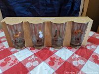 Front view of the four Rae Dunn graphic glasses in original packaging showing winter-themed designs and corresponding words.