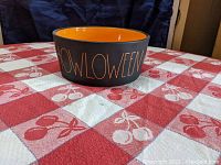Side view of Rae Dunn Halloween bowl showing 'HOWLOWEEN' lettering in orange on black matte exterior with orange glossy interior.