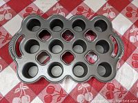 Top view of Nordic Ware petite popover pan showing 15 popover molds and two side handles on a red and white patterned cloth