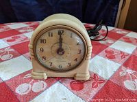 Front view of vintage beige Art Deco style alarm clock with visible clock face and power cord.