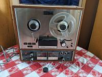 Front view showing wood veneer cabinet, silver metal faceplate, reel spindles and front panel layout.