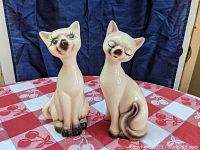 Front view of two porcelain Siamese cat figurines with detailed facial expressions and coloring.