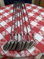 Photo showing the full set of seven left-handed golf irons numbered and laid out.