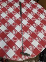 Full-length image of the golf putter on a red and white checkered tablecloth showing short shaft and club head.