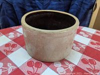 Stoneware crock side view showing beige salt-glazed exterior and round shape on red and white patterned cloth.