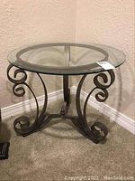 Full view of round glass top table with metal base and decorative scroll legs