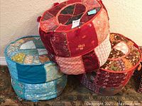 Three round patchwork pillow seats stacked and placed on a patterned rug.