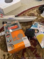 White and red NIKKO Torpedo Stinger II RC boat with remote control, orange inflatable lounger in box, blue and white inflatable tube and ball in clear packaging on carpeted floor.