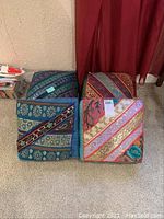 Four decorative pillow topped seats arranged on carpet with red curtain backdrop.