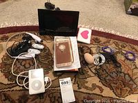 Overview photo showing all items including digital photo frame, iPod with charging cord, wired earbuds, phone cases, and miscellaneous accessories.