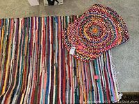 Photo showing two rugs laid on carpet: rectangular multicolored striped rug with fringe and round braided multicolored rug.