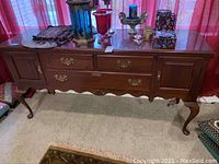 Full view of the wooden Ethan Allen buffet cabinet showing drawers, cabinet doors, brass hardware, and carved legs.
