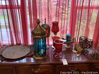 Wide shot showing two woven cases, beaded mat, three red candle holders, one blue candle holder, stained glass candle holder, small decorative candle holder and butterfly ornament on wooden furniture