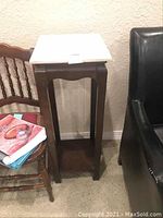 Full view of one marble topped plant stand showing white marble tabletop and wooden legs.