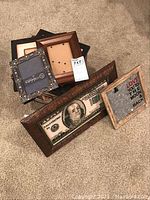 Assorted wooden and metal photo frames including a framed $100 bill print and a frame with metal clip and text.