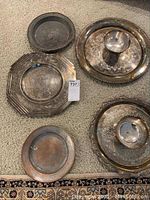 Overview of five silverplate and metal serving pieces on carpeted floor, showing trays and plates with varying shapes and signs of wear.