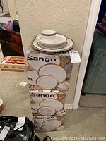 Three boxed sets of Sango Empress Gold 20-piece translucent china, stacked with one set plated on top showing a dinner plate, salad plate, cup and saucer.