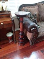 Full view of the wooden pedestal next to a sofa and piano with a candle on top.