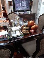 Full view of nine decoration pieces on a wooden dining table including candleholders, cupcake stands, ceramic vases, and brass swan figurine.