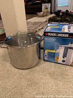 Photo of large stainless steel stock pot with lid next to Black & Decker juice extractor box on carpet.