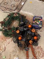 Photo showing a Christmas wreath with pine cones and berries, a Halloween wreath with black mesh, pumpkins, witch hat, and striped bow, and the boxed Star Shower Laser Magic laser light
