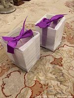 Two white boxes wrapped with purple ribbon, sealed and unopened.