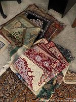 Assortment of folded fabric pieces including pillow covers and small rug with Middle Eastern patterns on carpeted floor