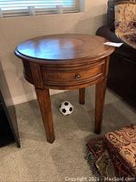 Full view of the round solid wood table with one drawer and four legs standing on carpeted floor.