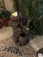 Full view of electric water feature showing three jugs and rock-like base on carpeted floor.