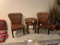 Photo showing a pair of two brown velvet patterned chairs with button tufted backs and curved wooden legs with a small round wooden table between them.