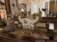 View of all three pieces on a brown marble table including large decorative urn, smaller urn, and statue.