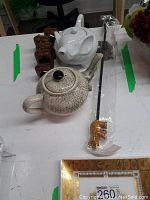 Photo of two ceramic teapots (one elephant-shaped white, one crackle-glazed beige), five wooden elephant napkin rings, and one wooden elephant backscratcher in package.