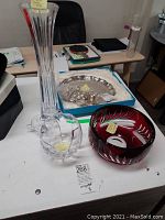 Photo showing tall clear Atlantis crystal vase with globe base next to Bohemia deep red crystal bowl with feather-like cut design.