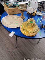 Overview of lot items on blue table including pottery platter, footed bowl, ceramic lamp shade, Asian screen, and other small items.