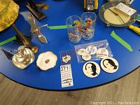 Metal bird sculpture, Trudeau related pins and buttons, two Disney themed drinking glasses on blue table