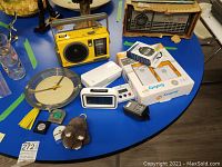 Various radios, Braun wall clock, digital stopwatches, D-Link device, and small items on a blue surface.