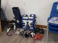 Overview of lot showing golf bag, goalie pads, skates, gloves, baseball glove, tennis racket and shoes.