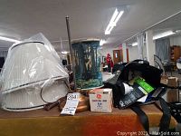 Overview photo showing the two pleated lampshades wrapped in plastic, cylindrical scene lamp with cracked paint, and some light bulbs on table surface.
