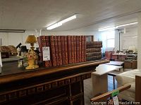 Wide shot showing 13 vintage books with burgundy leather covers on a wooden fireplace mantel.