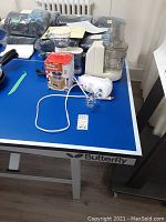 Table with the food processor, manual coffee grinder box, electric coffee grinder, and handheld egg beater all placed on a blue table.