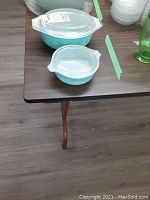 Two covered Pyrex casserole dishes on table, one large oval and one smaller round, both light blue with glass lids.