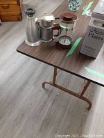 Photo showing both the French press with brown plastic parts and the Vesuviana Italian coffee maker made of metal with black handles on a table.